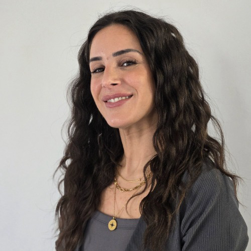 Headshot of Reham. Long wavy brown hair with a gray sweater and gold necklace